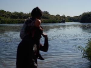 Migranti durante il pericoloso guado del fiume Del Rio. Molte anche le donne e i bambini (Ansa)